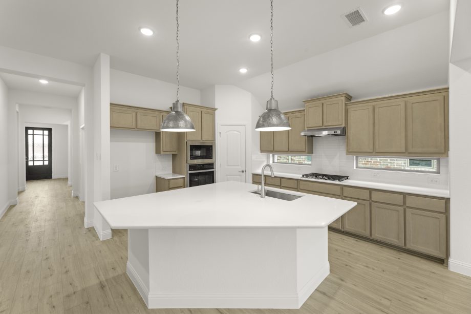 View of home entry and kitchen with optional kitchen island, pendant lighting, and light stained cabinetry.