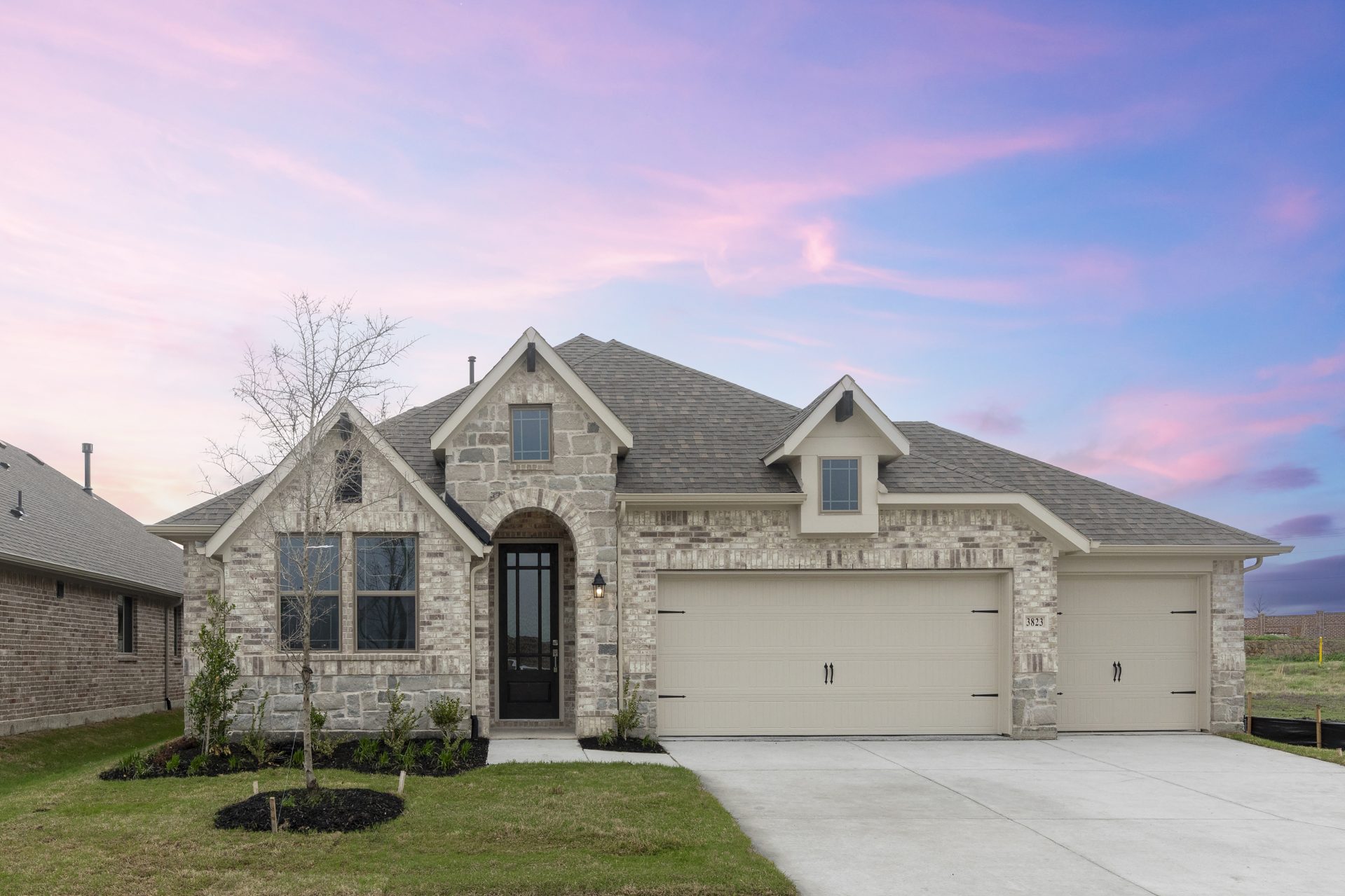 Front elevation of 3823 Brewster Lane in Royse City. This home showcases a light brick and stone exterior and a three car garage.
